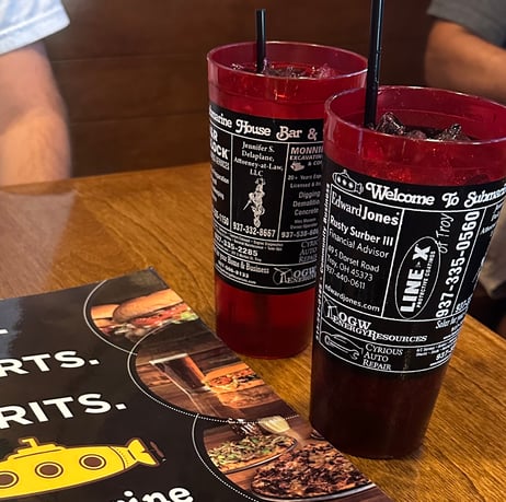 2 red cups filled with advertisements beside a restaurant menu for a place called Subhouse