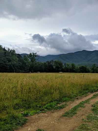 Cloudy sky above the Smokey Mountains of Tennessee, USA along a dirt path and field.